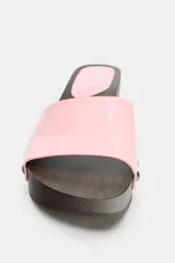 Sandalia de tacón tipo zueco con suela de madera oscura y plataforma, tira delantera ancha en material sintético rosa de efecto acharolado con tachas metálicas decorativas a los lados.