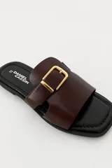 Sandalias planas color borravino con tiras cruzadas y hebilla dorada decorativa en el empeine.