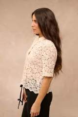 Camisa de encaje color crema, con cuello camisero, mangas cortas y cierre frontal con botones.