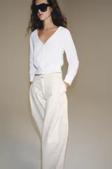 Top de algodón blanco de manga larga, con escote en V y cierre frontal con botones. Presenta bajo y puños en rib elástico.