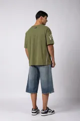 Remera de corte oversize color verde oliva con estampado frontal estilo universitario y detalles de líneas blancas en los hombros y laterales.