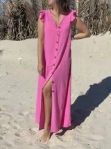 Vestido largo fucsia de lino, con corte recto, breteles anchos con volados y botones frontales. Presenta un tajo lateral.