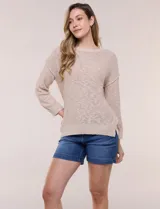 Buzo liviano de algodón con tejido de punto abierto y semi holgado, color beige, con escote bote, mangas largas de hombros caídos y costuras expuestas.