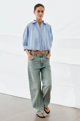 Camisa de algodón con cuello solapa, mangas abullonadas por debajo del codo y bajo acabado en globo. Presenta cierre frontal con botones ocultos.