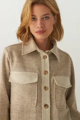 Camisa estilo leñador color beige con textura en espiga, de manga larga, con cuello clásico, cierre frontal con botones, dos bolsillos de parche con solapa abotonada en el pecho y puños abotonados. Confeccionada en lana fina sin teñir.