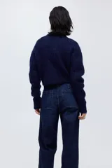 Pantalón de jean estilo wide leg con tiro alto, confeccionado en denim de algodón con leve stretch. Presenta cierre frontal con doble botón metálico, pliegues frontales y traseros, y bolsillos traseros de parche.