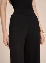 Pantalón negro de tejido de punto con corte recto, cintura alta, aberturas laterales y acabado acanalado.