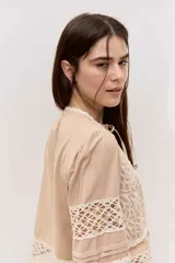Blusa tostada con mangas tres cuartos, detalles de encaje floral calado y cierre frontal con lazos.