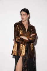 Chaqueta estilo blazer color bronce de cuero sintético con solapa y cuello de corderito desmontable. Presenta flecos en la delantera y en la espalda, dos bolsillos laterales y aberturas en los costados.