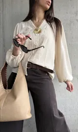 Camisa beige de manga larga con diseño abullonado y puños elastizados, escote en V con botones frontales y sutiles bordados florales tono sobre tono.