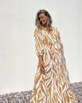 Túnica larga de corte holgado con estampado animal print tipo cebra en tonos beige y crudo. Presenta escote en V con cordones ajustables, mangas tres cuartos y falda con volados en el ruedo.