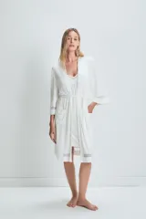 Bata de estar por casa color blanco, confeccionada en tejido suave con caída fluida. Presenta mangas tres cuartos con detalles de transparencias en los puños y el ruedo, bolsillos laterales y un lazo ajustable en la cintura.