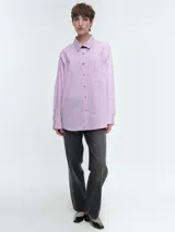 Camisa oversize de popelina de algodón con diseño de rayas verticales, cuello clásico, cierre frontal con botones, manga larga con puños anchos y bolsillo aplicado en el pecho.