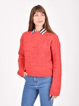 Buzo de tejido de punto trenzado color rojo, con cuello redondo y puños y ruedo acanalados. Se lleva sobre una camisa de cuello a rayas blancas y azul marino.
