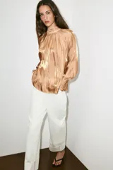 Camisa satinada color tostado con cuello alto fruncido, mangas largas amplias y puños elásticos con volados.