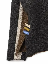 Polera de tejido lambswool con diseño bicolor en tonos neutros. Presenta cuello alto tejido, mangas largas con franjas laterales en color marrón y detalle de bordado artesanal con tres pequeñas líneas horizontales en colores vibrantes.