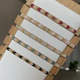 Pulsera artesanal confeccionada con cuentas Miyuki en tonos beige, dorado y detalles en rojo, con diseño ajustable.