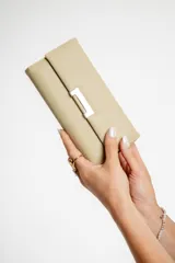 Monedero tipo sobre color beige, con cierre de broche metálico plateado. Interior con tarjetero, espacio para billetes y bolsillo con cierre.