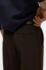 Pantalón de corte relajado color marrón, con cierre de botón, cintura con elástico y cordón interno, bolsillos laterales al bies y bolsillos traseros ribeteados con botón.