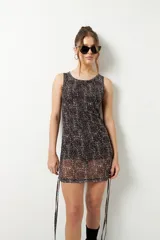 Minivestido sin mangas con estampado tie-dye en tonos beige y negro. Confeccionado en microtul con leve transparencia y cordones ajustables en los laterales.