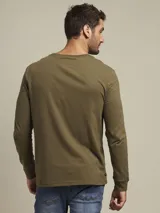 Remera de manga larga color verde militar, con cuello redondo y logo bordado de un pájaro en el pecho.