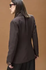 Blazer sastrero color chocolate con solapas clásicas, cierre frontal y bolsillos con tapa. Presenta detalles de encaje negro en los puños.