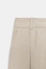 Pantalón de tiro medio color beige, con pinzas delanteras, bolsillos frontales y pernera recta. Cuenta con cierre frontal con cremallera, botón interior y gancho.