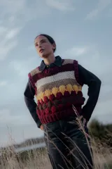 Chaleco tejido de punto con diseño de rayas horizontales y bloques de color en tonos bordó, beige, blanco y amarillo. Presenta cuello redondo y terminaciones acanaladas.