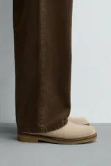 Bota estilo Chelsea de hombre, confeccionada en piel con acabado de serraje en color beige. Presenta elásticos laterales al tono, horma redonda y suela de goma a contraste con ligero tacón.