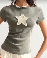 Remera verde oliva de algodón con cuello redondo y manga corta. Tiene un aplique de estrella en el frente y detalles de ojales metálicos en las mangas.