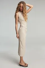 Vestido midi de cuello subido y sin mangas, confeccionado con un diseño drapeado lateral que aporta textura y movimiento a la prenda. Presenta un corte entallado y cierre de cremallera oculta en la espalda.