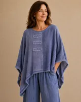 Blusa azul jean de corte holgado y asimétrico, con cuello redondo, mangas amplias y detalles de bordes deshilachados en el ruedo, mangas y en tres apliques rectangulares frontales.