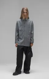 Camisa de manga larga en tejido twill color gris melange, con corte oversize. Presenta cuello clásico, cierre frontal con botones y tres bolsillos delanteros, uno de ellos oculto.