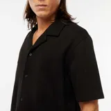 Camisa negra de manga corta con cuello solapa y cierre abotonado.