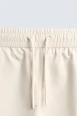 Bañador de hombre negro, largo hasta la rodilla, con acabado aterciopelado. Presenta cintura elástica ajustable con cordón, bolsillos laterales y un bolsillo trasero de plastrón. Incluye forro interior.