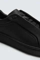 Zapatilla negra de cordones, con parte superior lisa y cordonera oculta. Posee suela con volumen a tono.