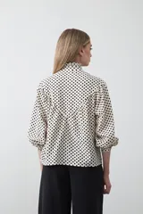 Camisa de viscosa con estampado de lunares, cuello alto con volados y cierre frontal de botones. Presenta un diseño de silueta suelta con frunces que aportan volumen y mangas largas con puños ajustados.