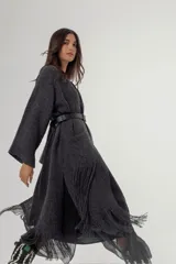 Saco largo de tejido de punto color gris oscuro, con mangas anchas, aberturas laterales y flecos largos en el ruedo. Presenta un diseño abierto que permite el uso de cinturón para entallar la silueta.