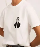 Blusa blanca de algodón con cuello redondo y mangas cortas. Presenta un estampado de una caricatura de una mujer con boina, lentes de sol y un trago en la mano.