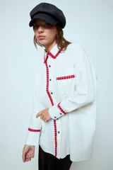 Camisa blanca de algodón con detalles de puntilla roja en cuello, solapa frontal, bolsillo y puños. Presenta botones en color celeste.