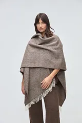 Ruana de lana sin teñir en tonos beige, con textura acanalada y terminaciones con flecos en los bordes.