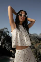 Conjunto de dos piezas compuesto por un top sin mangas de corte holgado y una falda corta acampanada, ambos confeccionados en lino con estampado de lunares dorados.