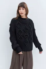 Sweater de punto grueso color rojo, con cuello alto y diseño de relieves tipo pompones en el frente y las mangas. Presenta puños y ruedo acanalados.