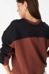 Buzo de cuello redondo con diseño de bloques de color en gris y negro, mangas largas y detalle bordado en el pecho.