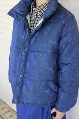Campera puffer de diseño capitoneado, confeccionada en tela impermeable con estampado multicolor de motivos marinos y cadenas. Presenta cuello alto, cierre frontal con botones a presión y puños elásticos.