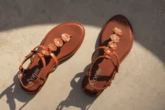 Sandalias bajas color hueso, con tira delantera con apliques de flores blancas y tira trasera con hebilla.