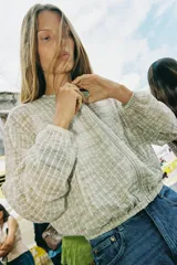 Cazadora de cuello redondo y manga larga, color verde claro con patrón a cuadros. Confeccionada en tejido de organza con estructura y acabados elásticos. Cierre frontal con cremallera y bolsillos delanteros.