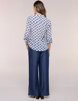 Camisa de gasa blanca con estampado de lunares en tonos azules, cuello con solapa, cierre frontal de botones, bolsillo aplicado en el pecho y detalle de nudo en el dobladillo inferior. Cuenta con mangas largas regulables.