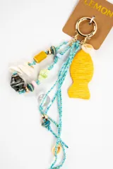 Charm para bolso con argolla dorada, cordones de hilo celeste y colgantes variados que incluyen cuentas de cerámica, conchas marinas, abalorios de cristal y un dije grande en forma de pez de color amarillo.