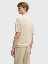 Remera polo de punto fino color beige, con cierre frontal parcial y cuello clásico. Presenta mangas cortas con terminación en rib y diseño de calce ajustado.
